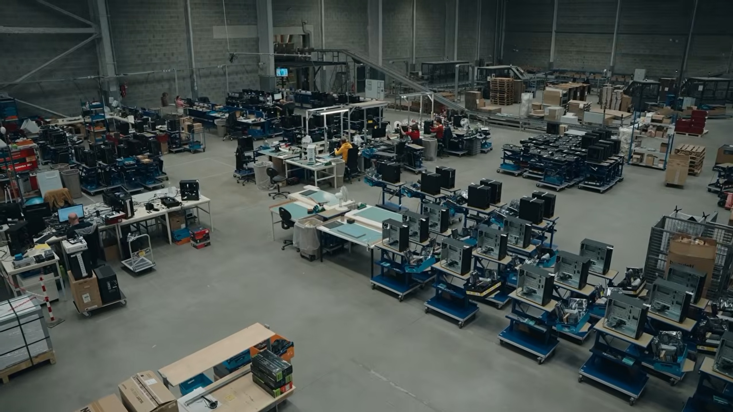 Vue d’ensemble d’un atelier d’assemblage informatique, avec des équipes aux postes de travail et des rangées de boîtiers de PC.